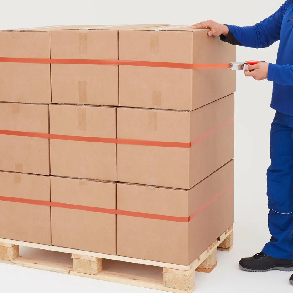 Detalle de la aplicación de cinta adhesiva de fleje con el aplicador manual tesa sobre un palet con cajas de cartón.